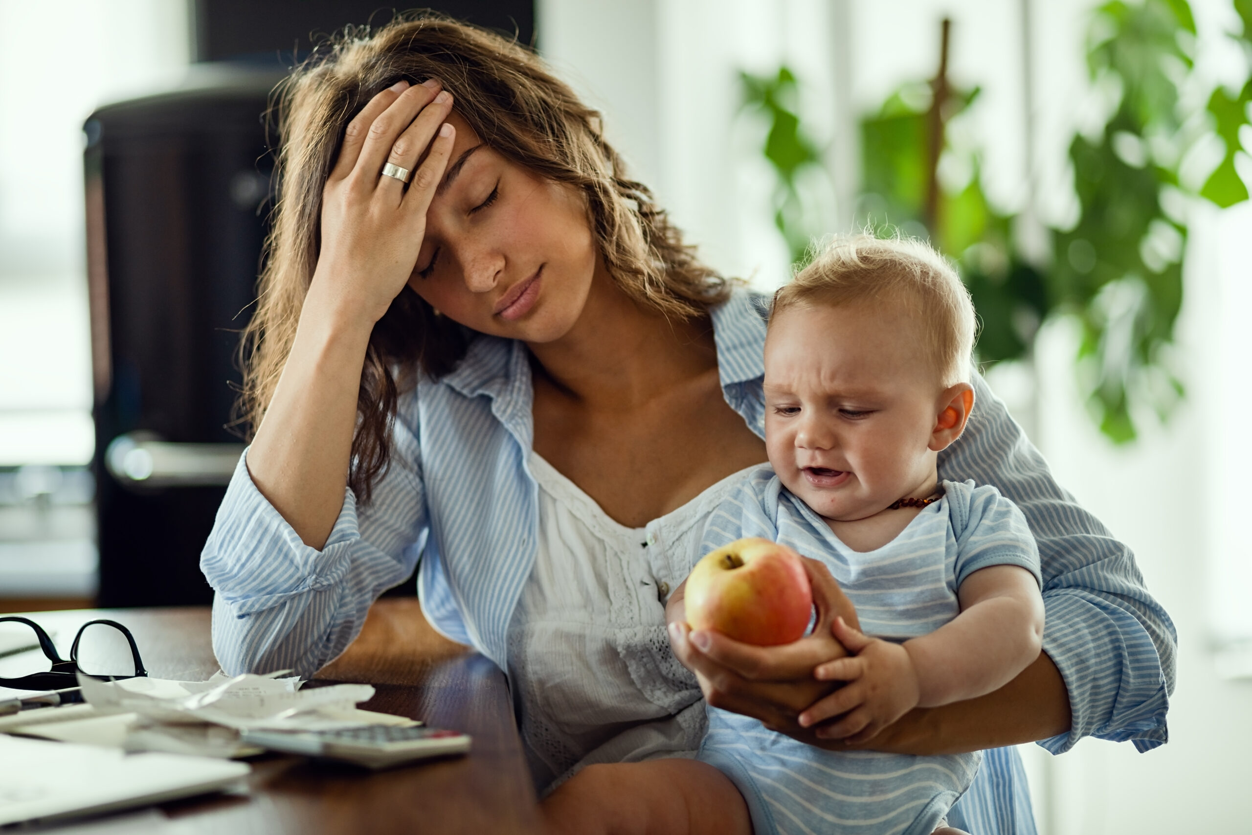 Young mother feeling exhausted while being with her baby and working at home.
