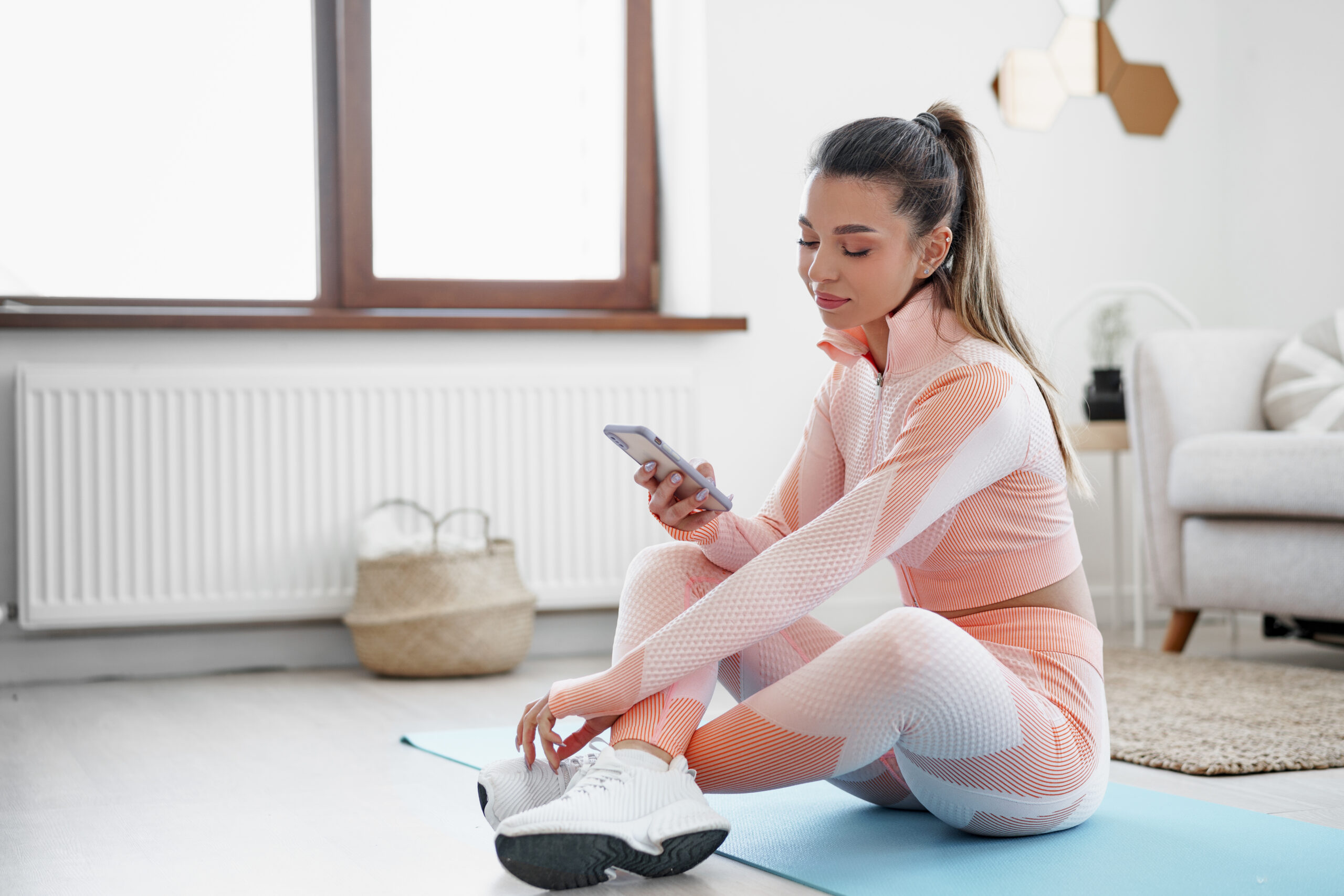 Beautiful young woman in sportswear sitting indoors and looking at smartphone before workout, close up