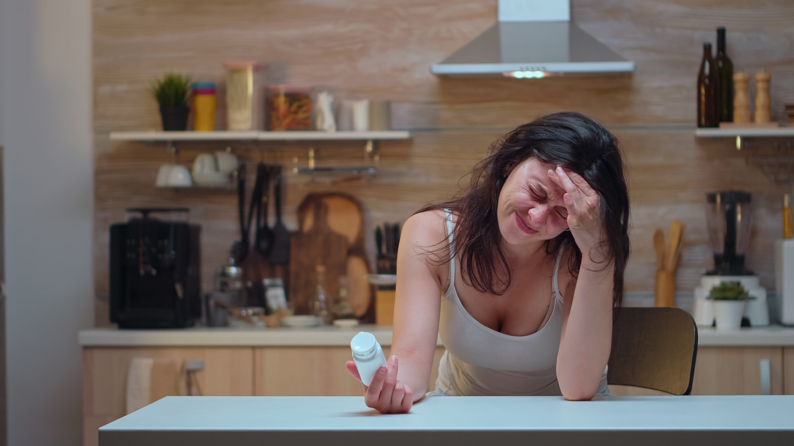 Wife with headache holding pills bottle reading the informations. Stressed tired unhappy worried person suffering of migraine, depression, disease and anxiety feeling exhausted with dizziness symptoms