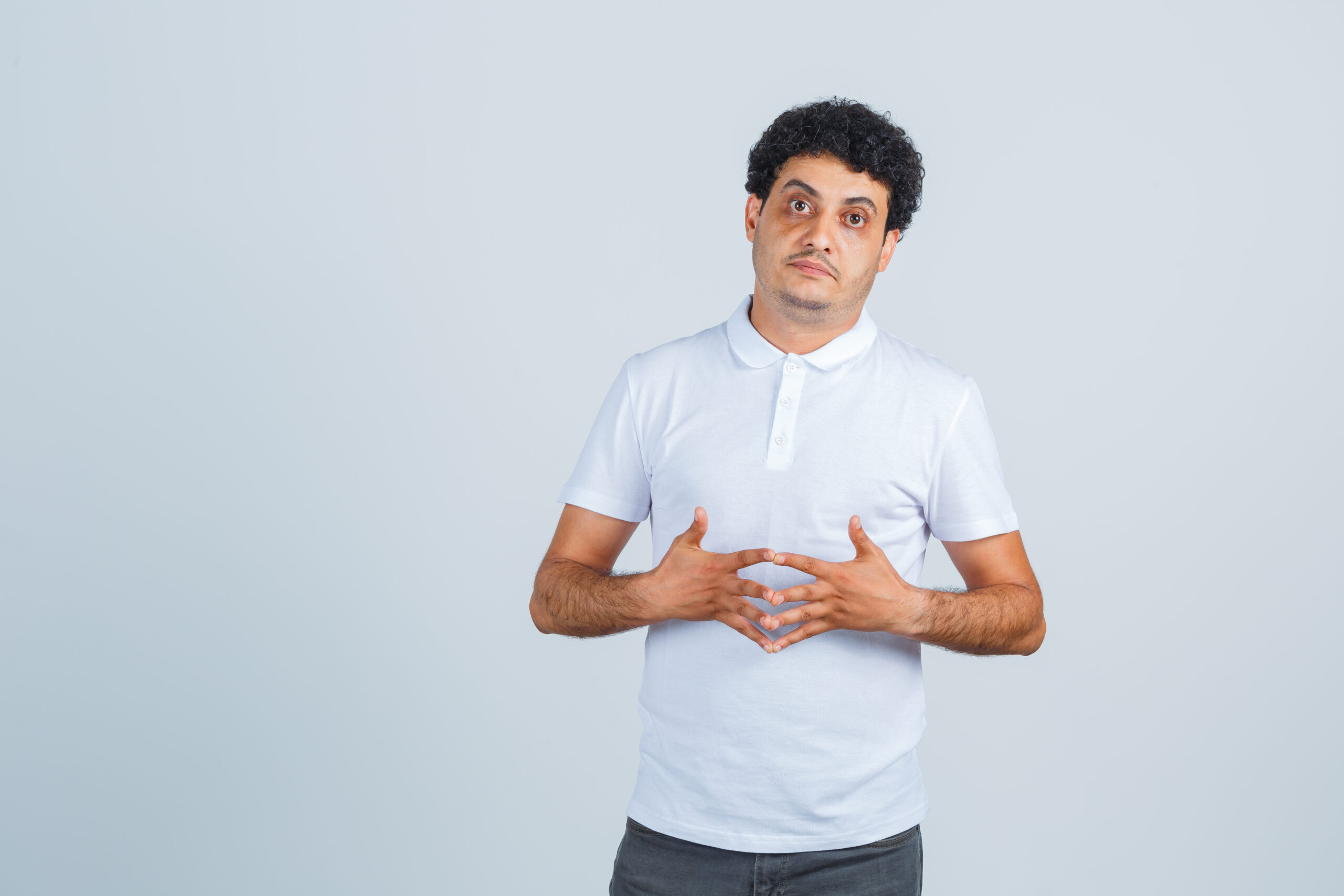 young man standing in thinking pose in white t-shirt, pants and looking sensible , front view.